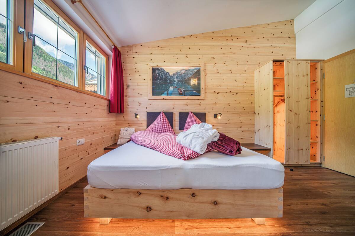 A wooden-paneled room with a bed, a painting, and a window with curtains.