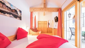 Un dormitorio con cama, almohadas rojas, cabecera de madera, un cuadro, un armario y una puerta corrediza de cristal a un balcón.