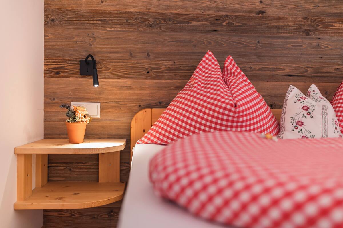 A bedroom with a wooden headboard, a bedside table with a potted plant, and red and white checkered pillows.