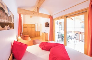 A bedroom with a large bed, wooden furniture, a TV, and a balcony with chairs. - Hotel Apartment Haus Gitschberg (Vandoies)