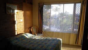 Una habitación con cama, una silla, un ventanal con cortinas y vistas al exterior.