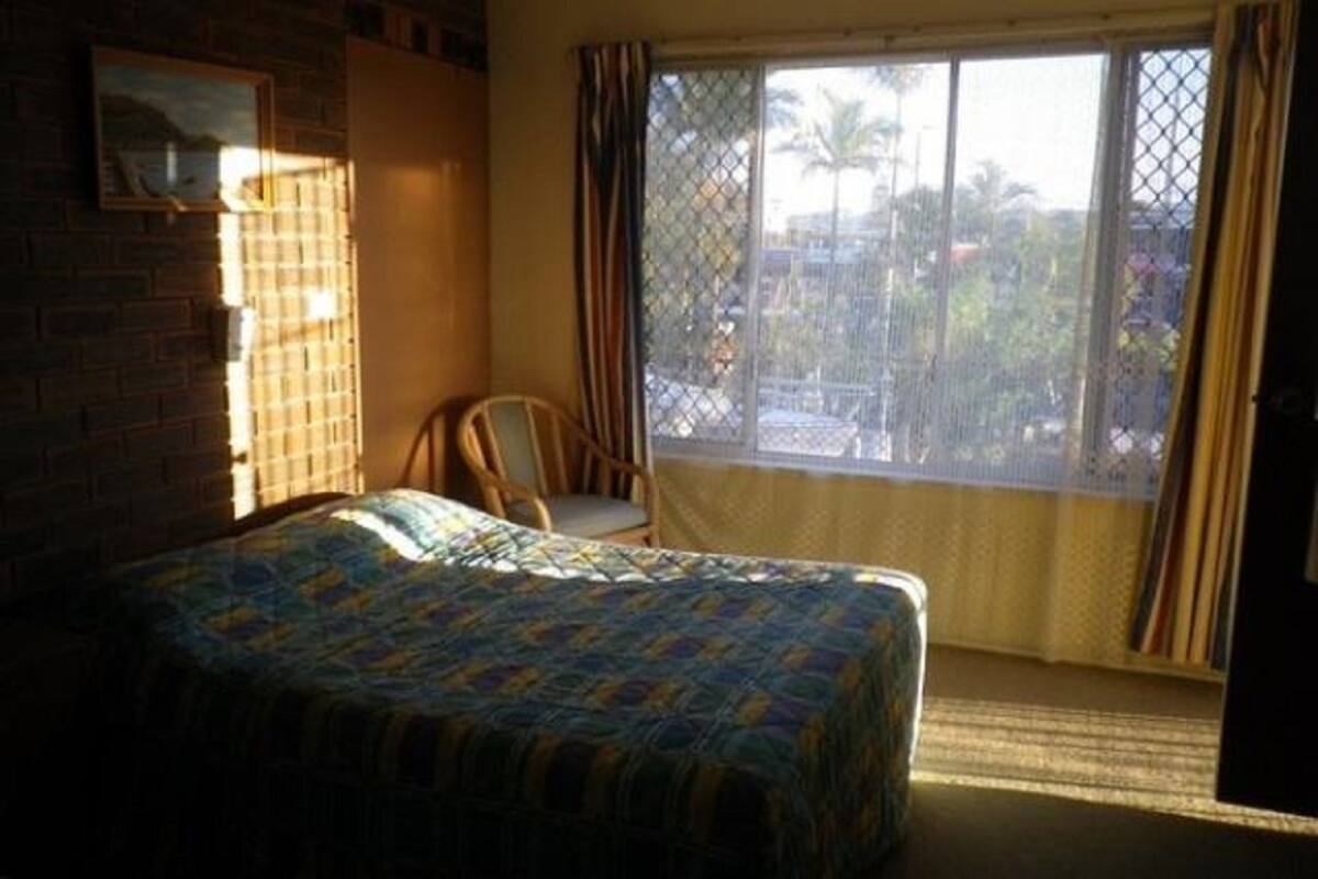 Une pièce avec un lit, une chaise, une fenêtre avec des rideaux et une vue sur l’extérieur.