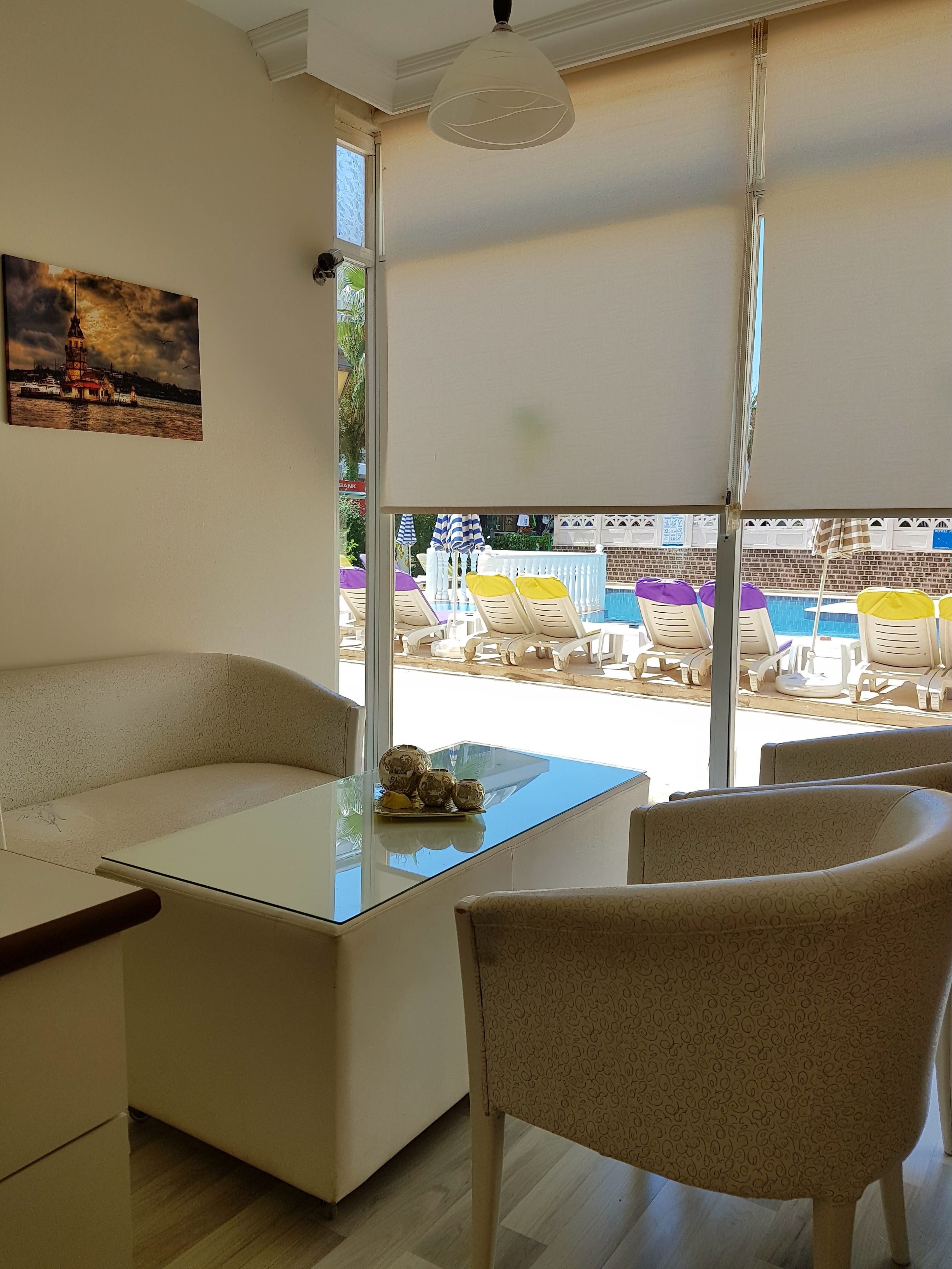 Una habitación con una mesa de vidrio, sillas de color beige con estampado, un cuadro en la pared y vistas a un área de piscina al aire libre.