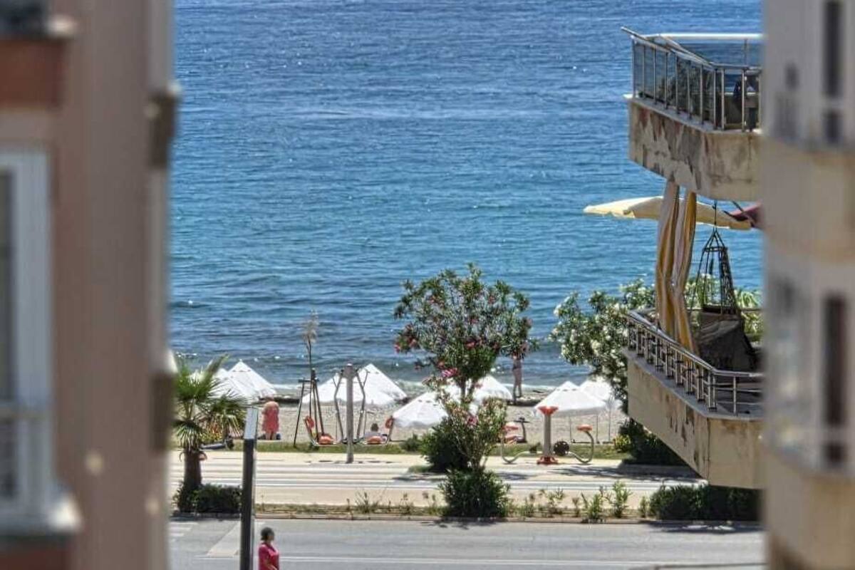 A coastal view with a building overlooking the sea, a pedestrian walkway, and outdoor seating.