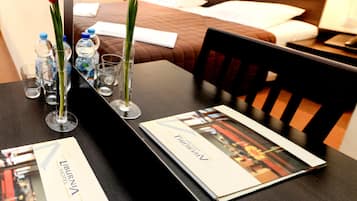Una camera d'albergo con un tavolo ordinato, con bottigliette d'acqua, bicchieri e una brochure.