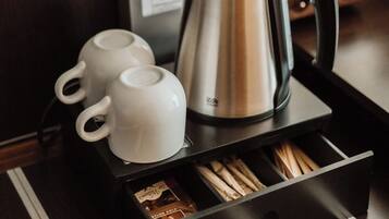 A coffee station with a kettle, two white cups, and a tray with tea bags.