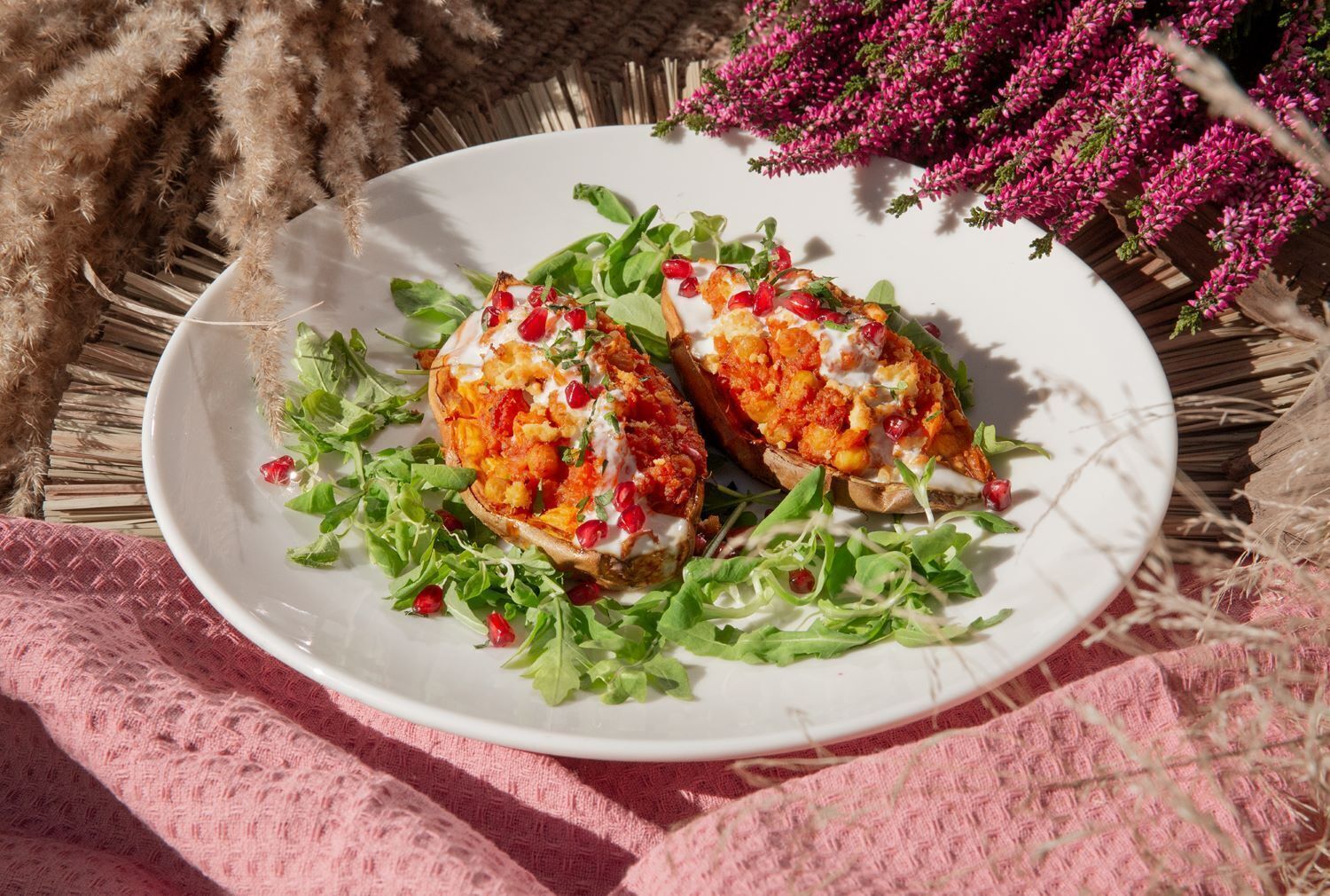 Un piatto di peperoni ripieni accompagnato da un'insalata, su un piatto bianco, posto su un tavolo ricoperto da una tovaglia rosa e decorato con fiori.