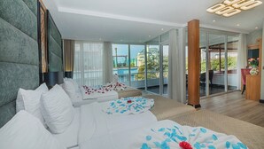 Habitación de hotel moderna con una cama grande, un sofá y un balcón con vistas a un paisaje urbano.