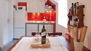 Cozinha com frigorífico, micro-ondas e painel de azulejos vermelhos. Há uma garrafa de vinho na mesa com copos.