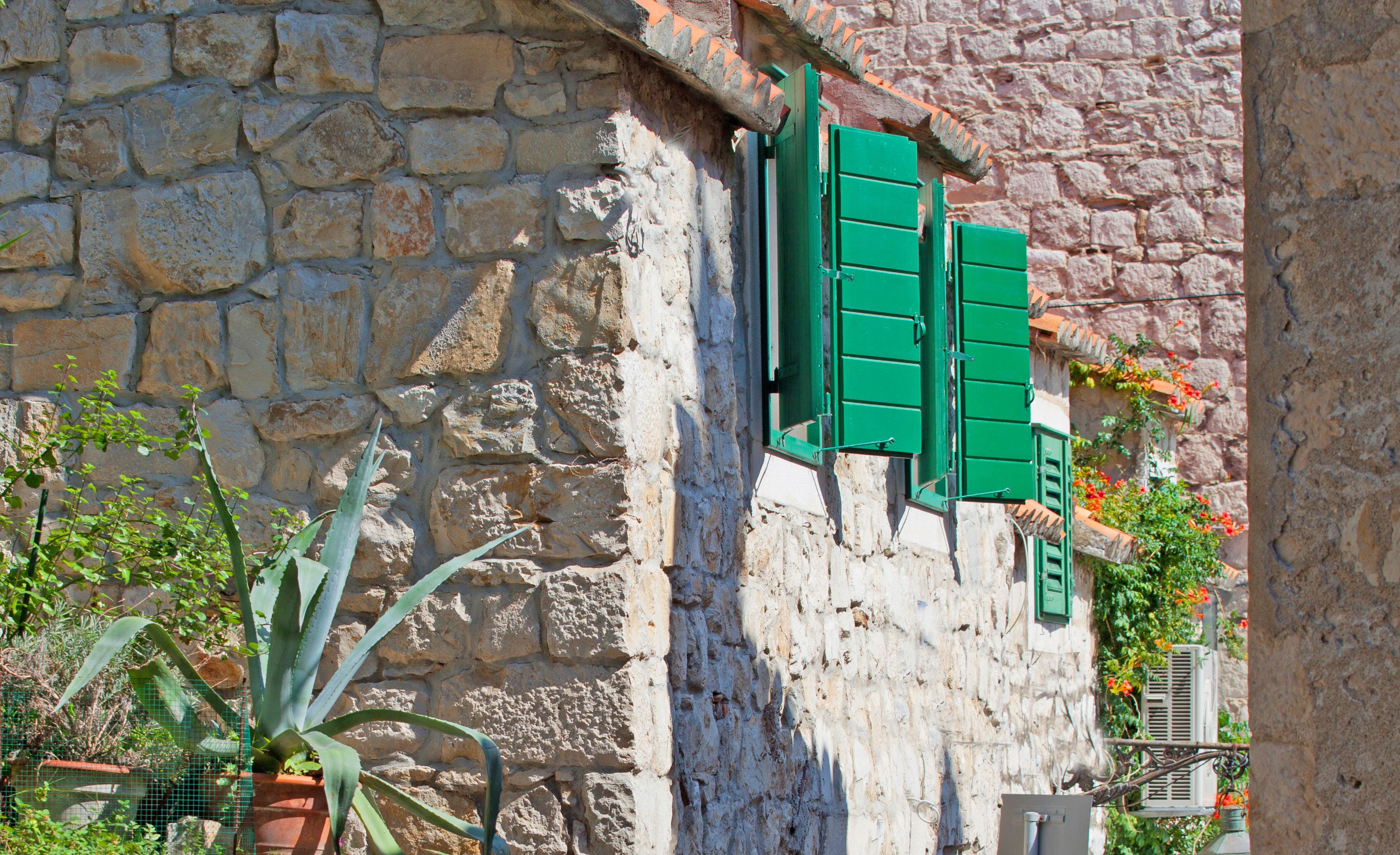 Un bâtiment en pierre avec des volets verts et un pot de fleurs.