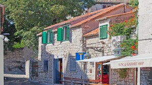 Um edifício de pedra com uma loja de vinhos e produtos gourmet, mesas ao ar livre e uma placa indicando estabelecimento local.