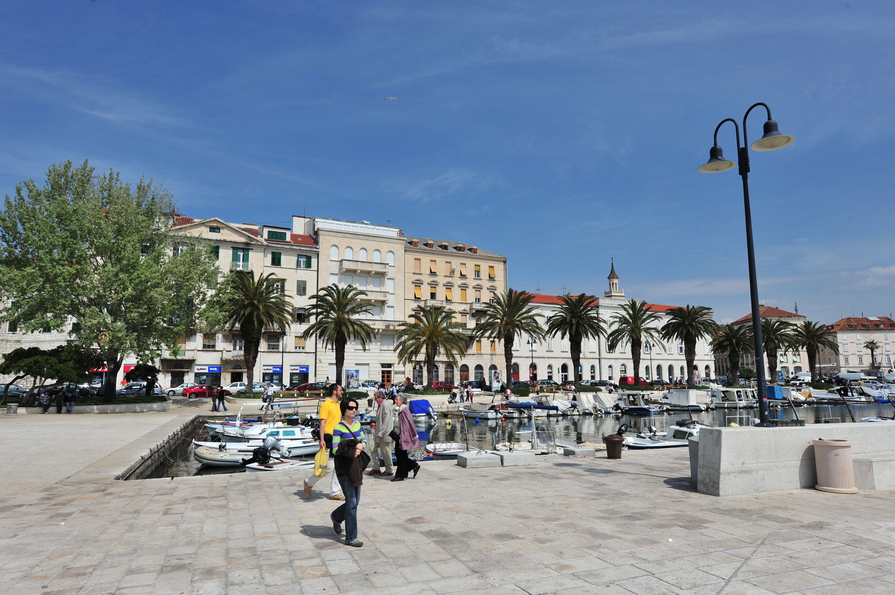 A public square with a marina, palm trees, and historic buildings.