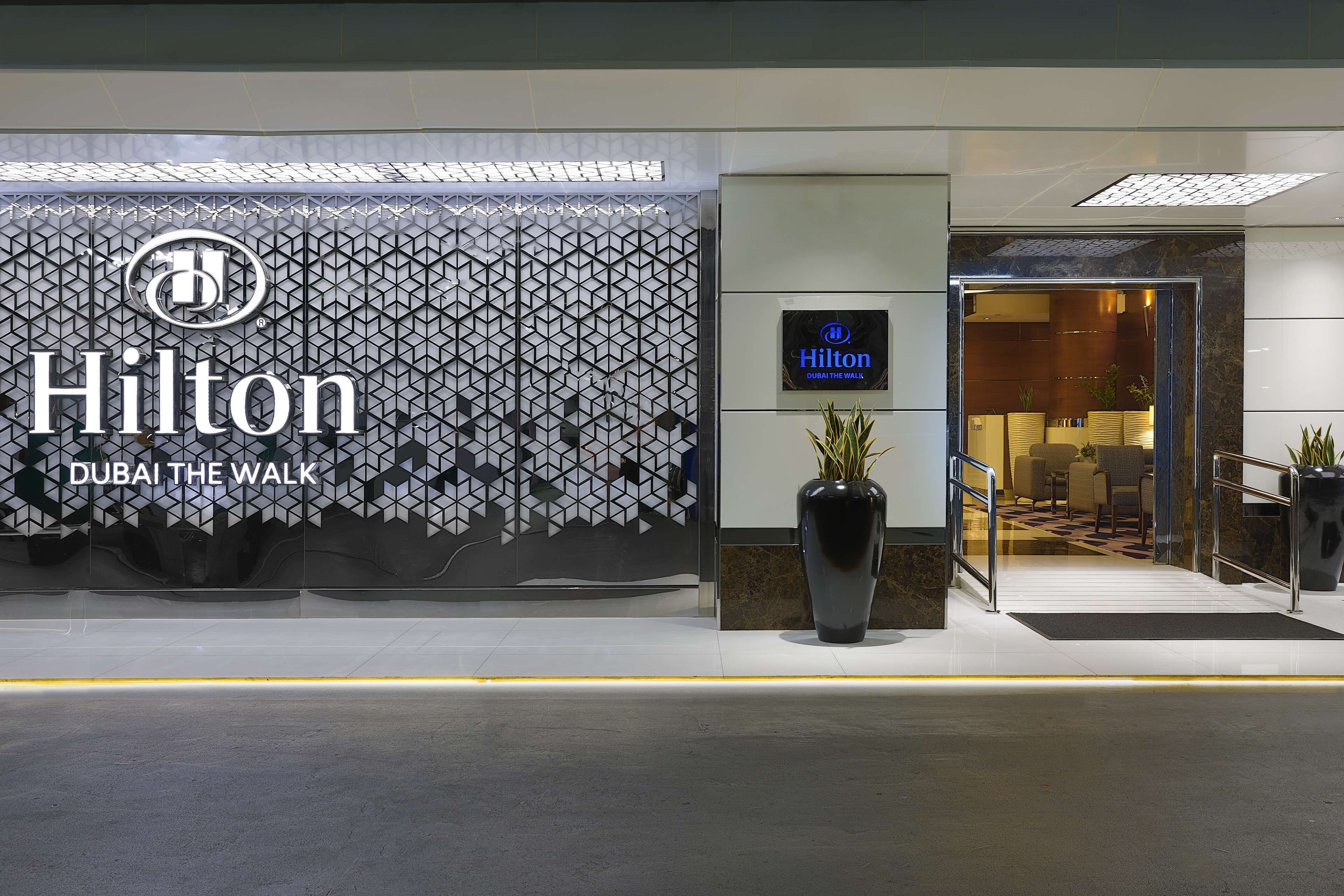 Entrada de un hotel Hilton con fachada de diseño geométrico y una planta grande en maceta.