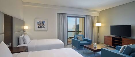 A hotel room with two beds, a sofa, a TV, and a balcony with curtains.