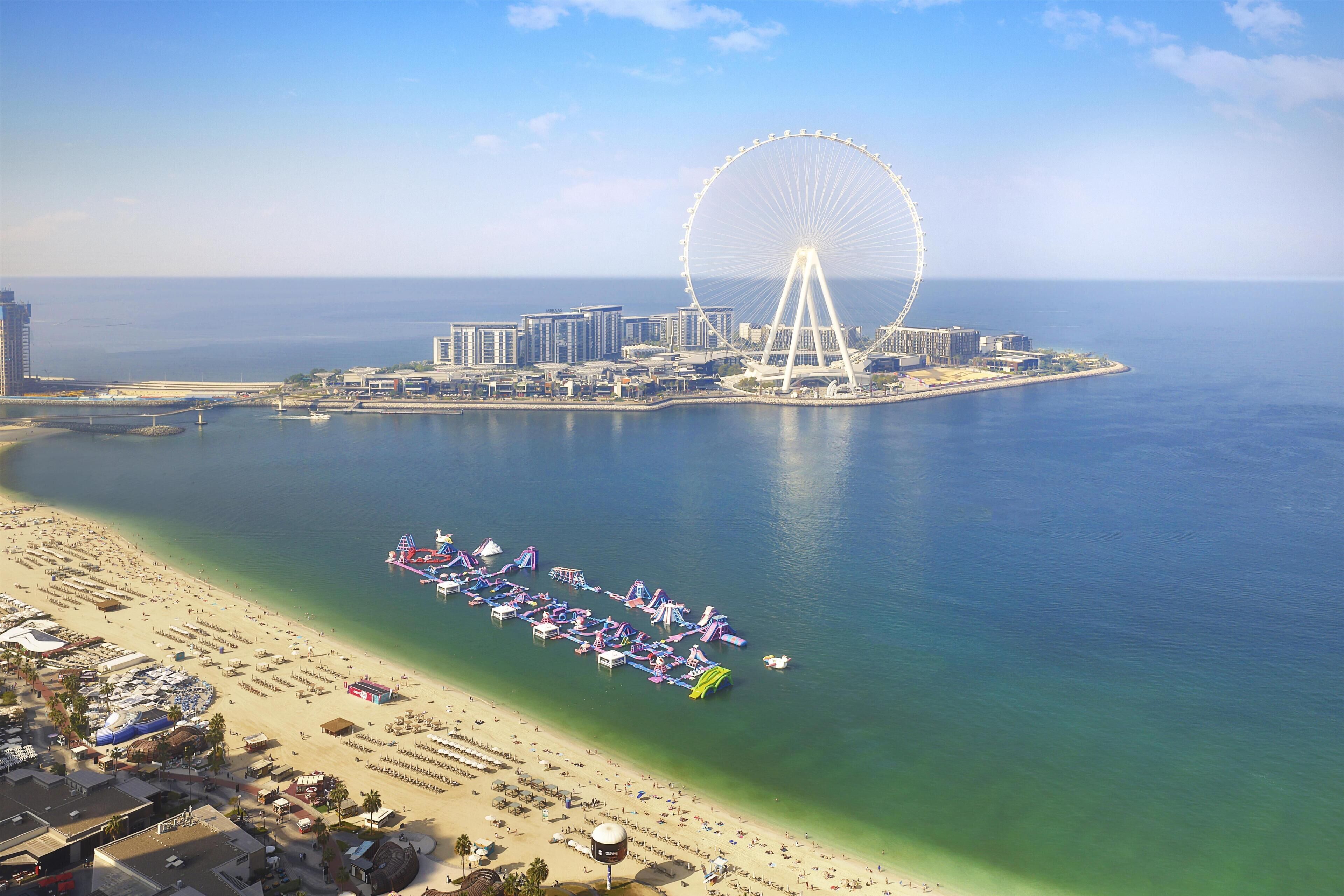 A coastal cityscape with a large Ferris wheel, a beach with umbrellas, and a marina.