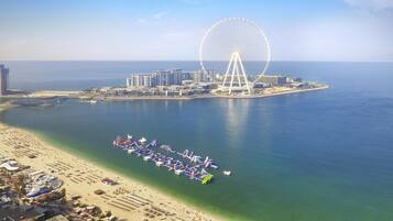 A coastal cityscape with a large Ferris wheel, a beach with umbrellas, and a marina.