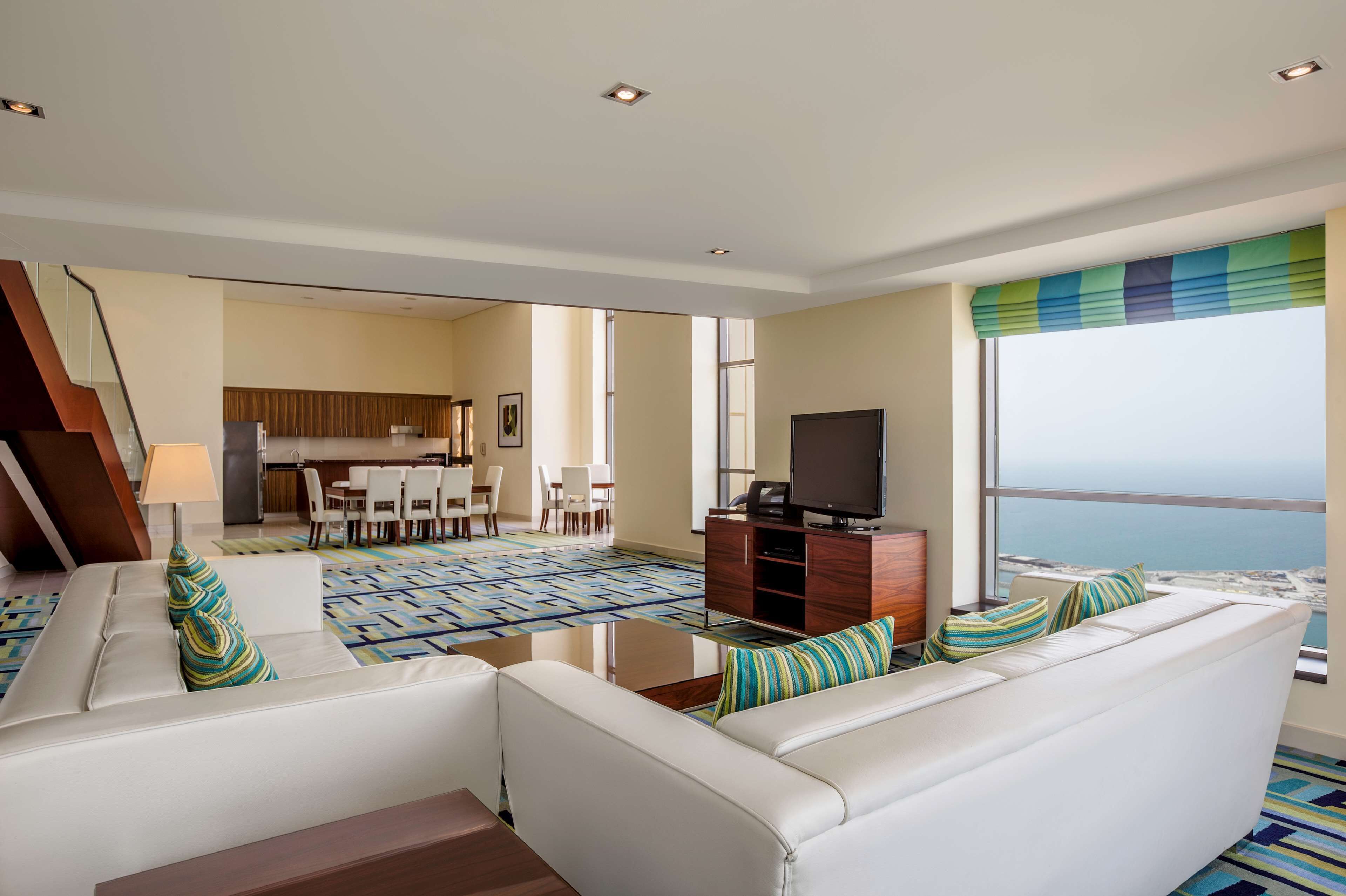 A modern living room with a white sofa, a flat-screen TV, and a view of the ocean.