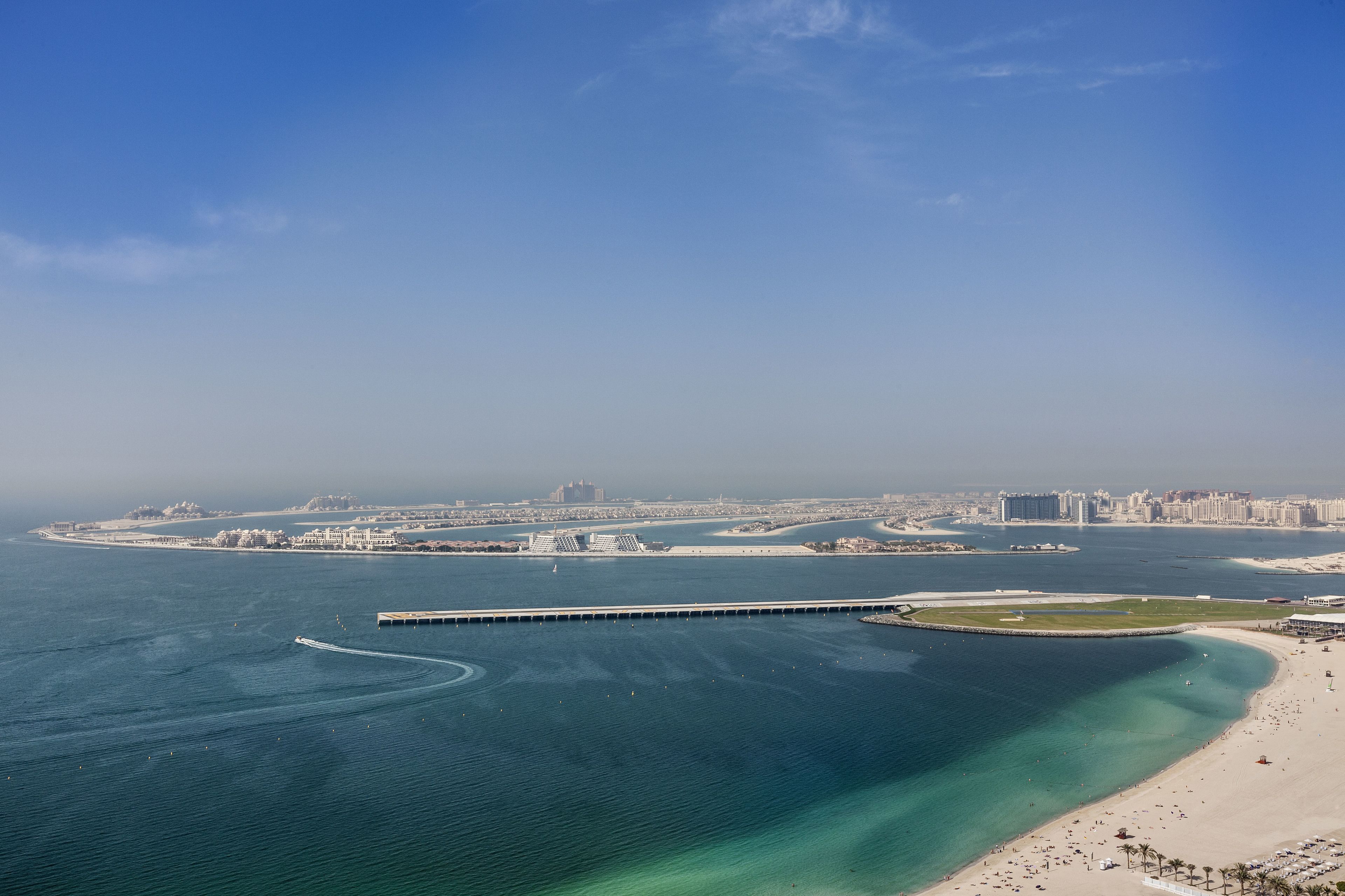 An aerial view of a coastal city with a marina, sandy beaches, and a clear blue sky.