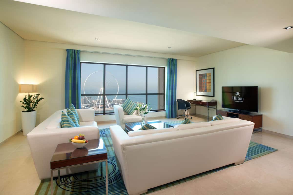A modern living room with a sofa, coffee table, and a TV. A large window offers a view of a Ferris wheel.