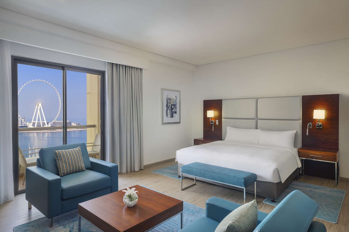 A hotel room with a large bed, a sofa, a coffee table, and a view of a Ferris wheel through the window.