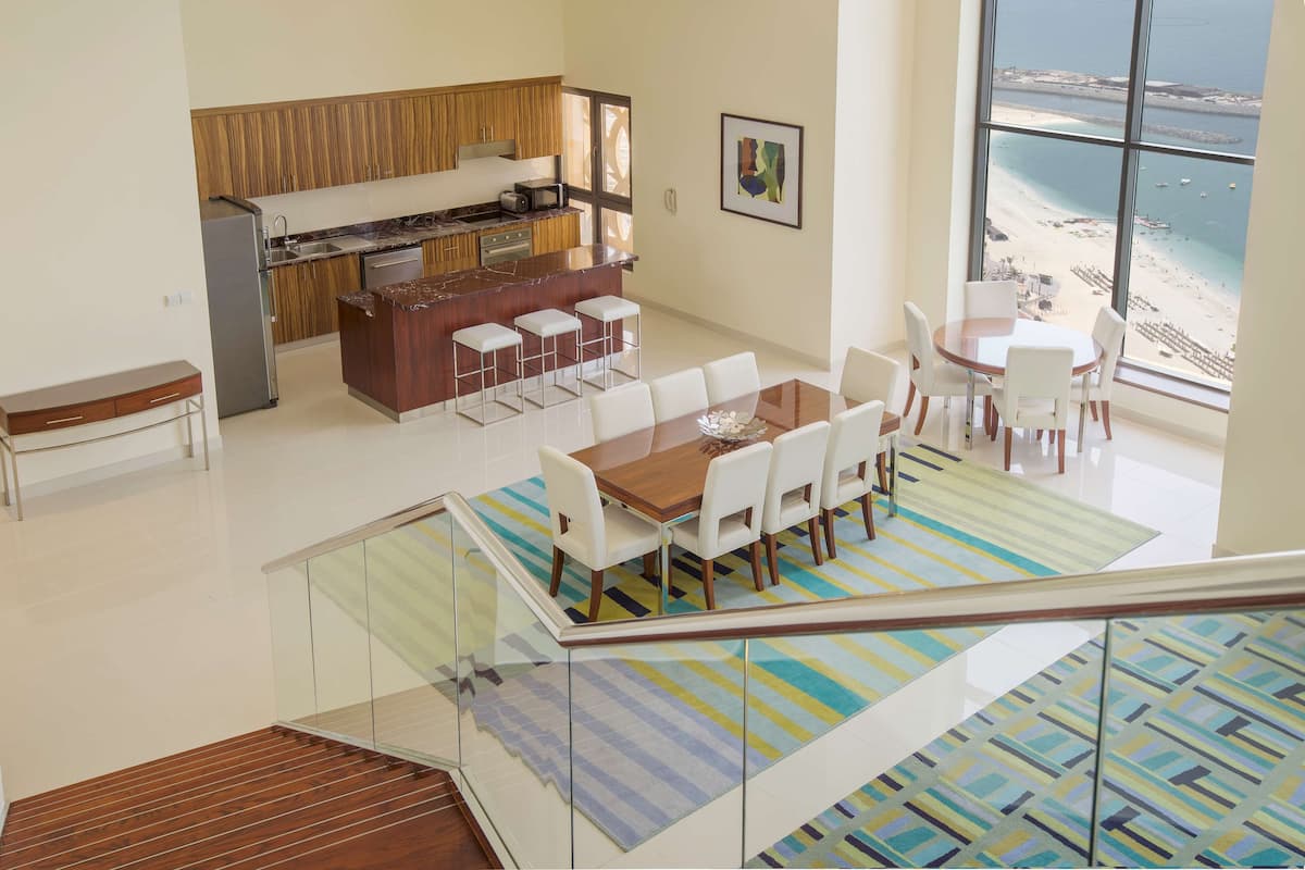 A modern kitchen with a bar area, dining space with a view of the beach, and a staircase with a patterned rug.