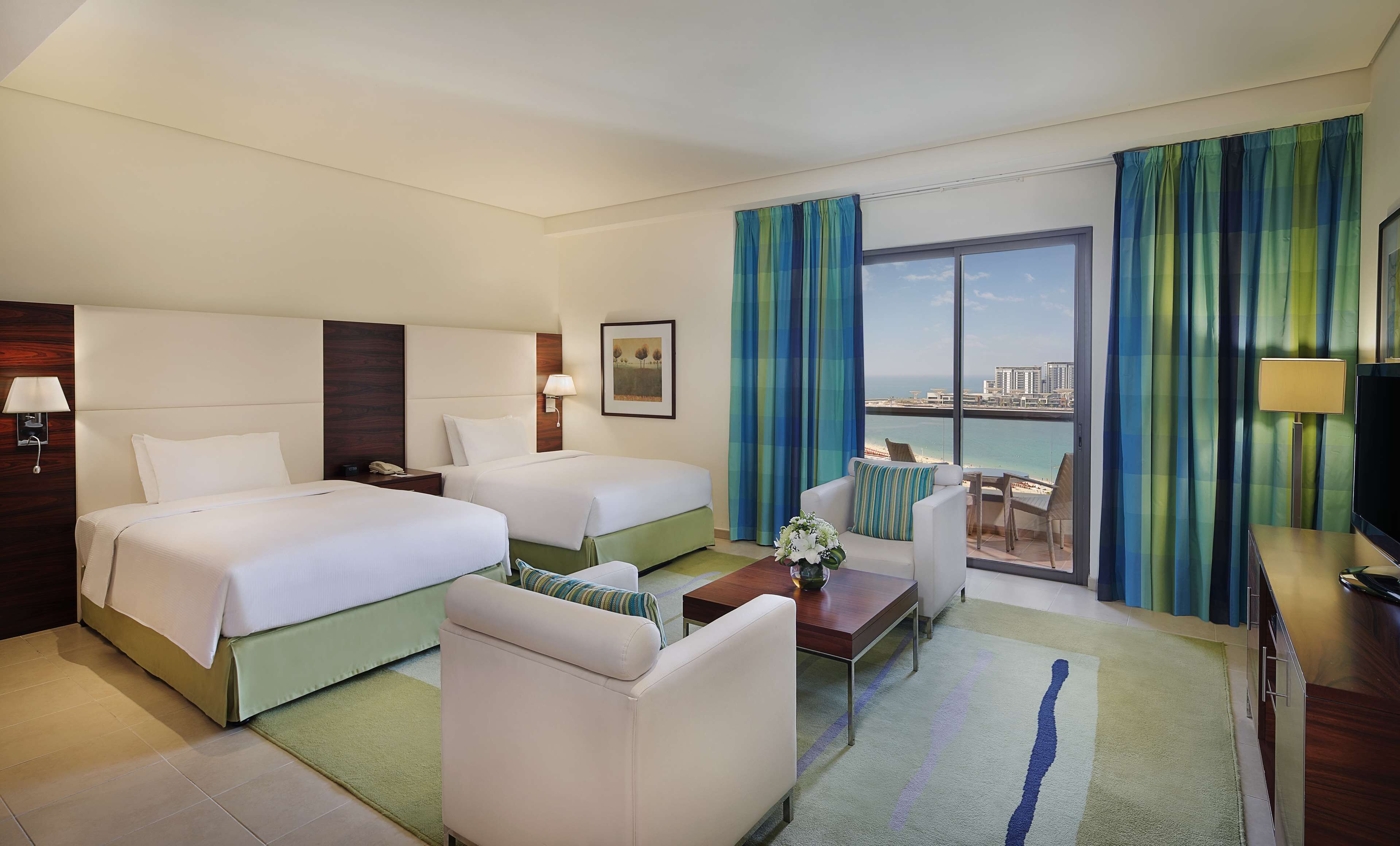 A hotel room with two beds, a sofa, a small table, and a view of the sea.