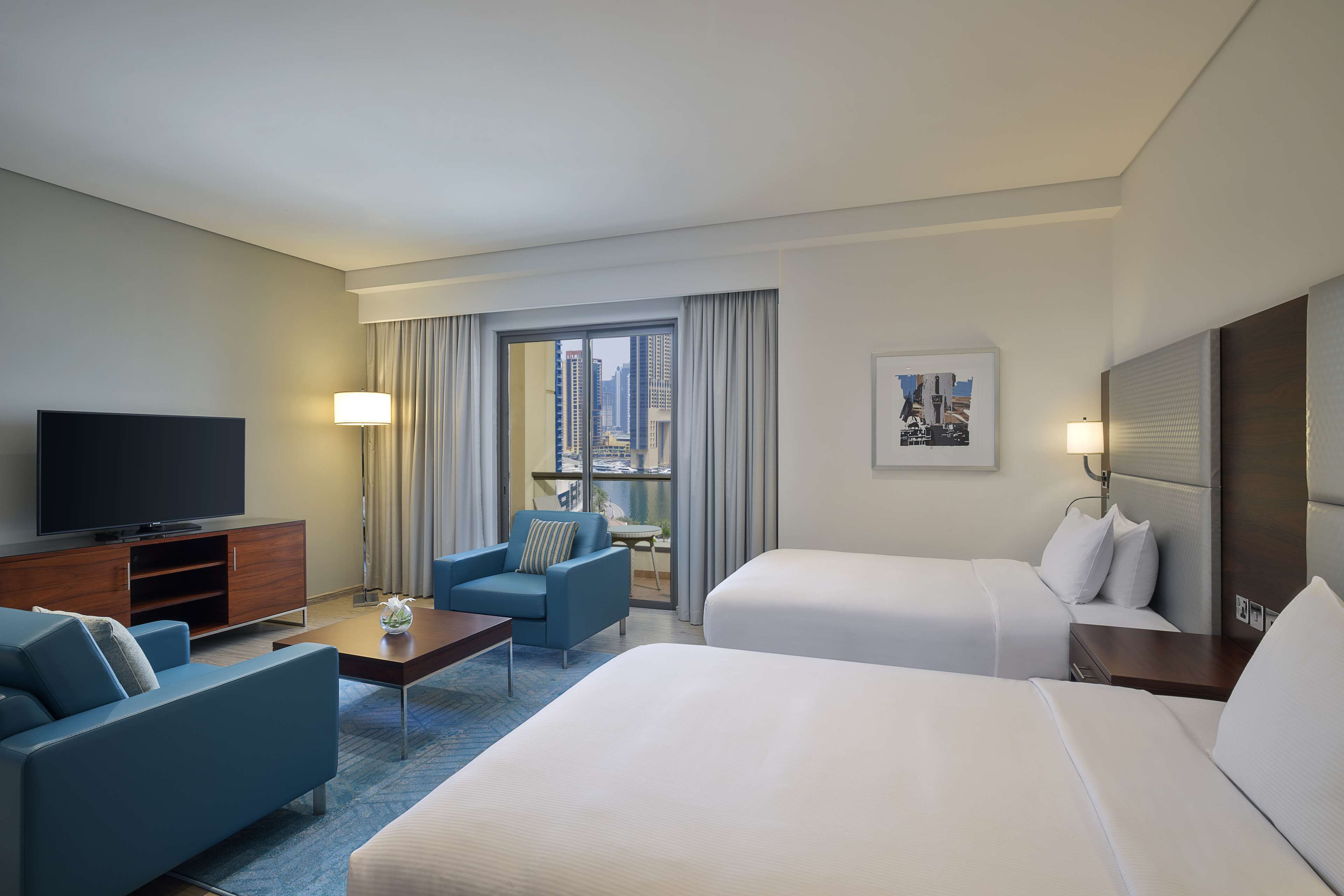 Ett hotellrum med en stor säng, en soffa, en TV och utsikt över staden.