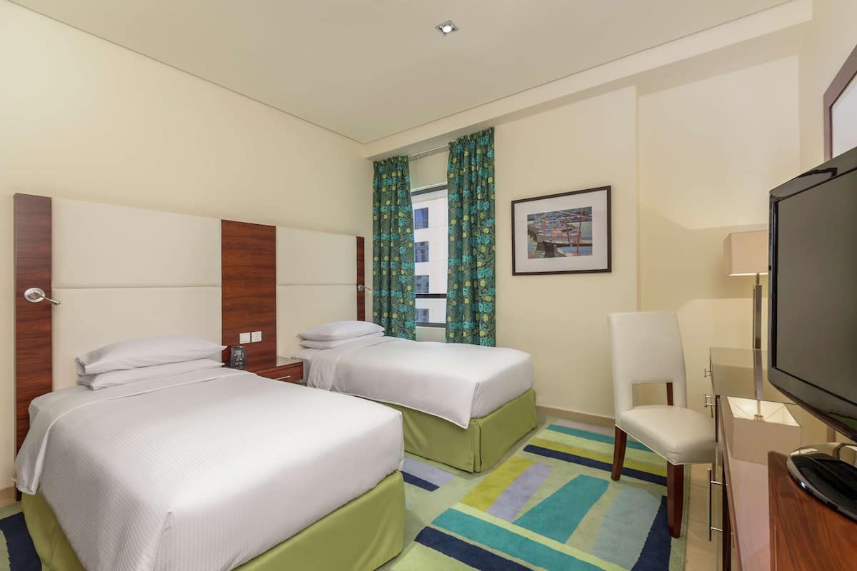 A hotel room with two beds, a television, a desk, and a chair.