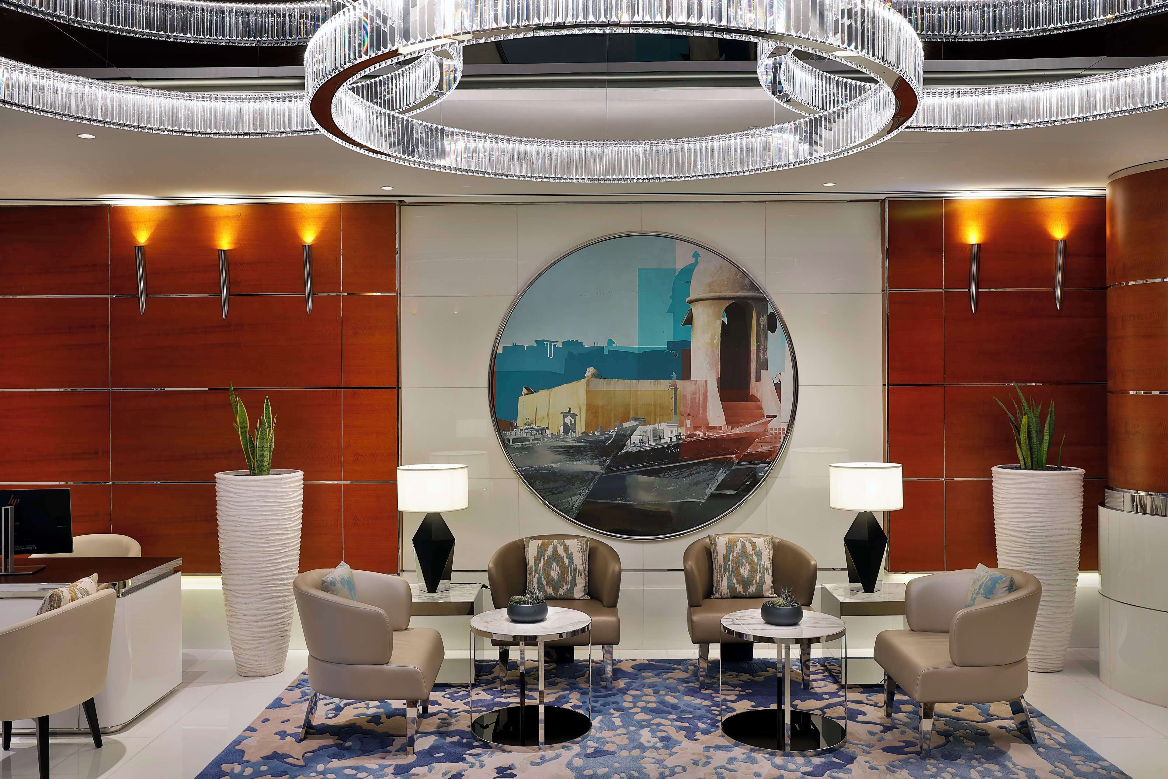 A modern lobby with a large round painting, two sofas, a desk, and a chandelier.