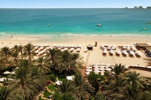 A beach resort with rows of sun loungers and umbrellas, palm trees, and a view of the ocean.