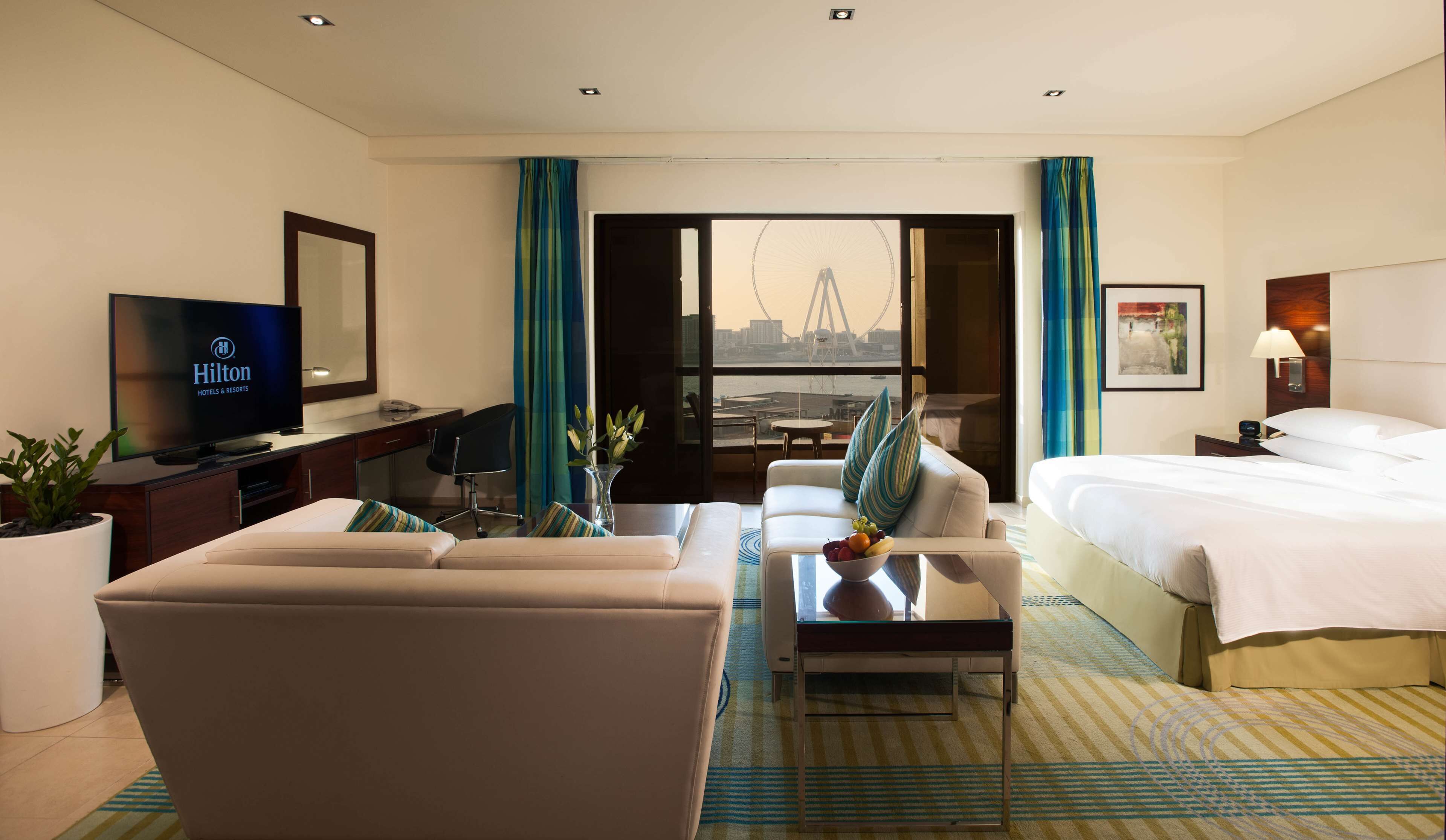 Hotelkamer met een bed, een bank, een bureau met een televisie, een stoel, een eettafel en uitzicht op een brug.