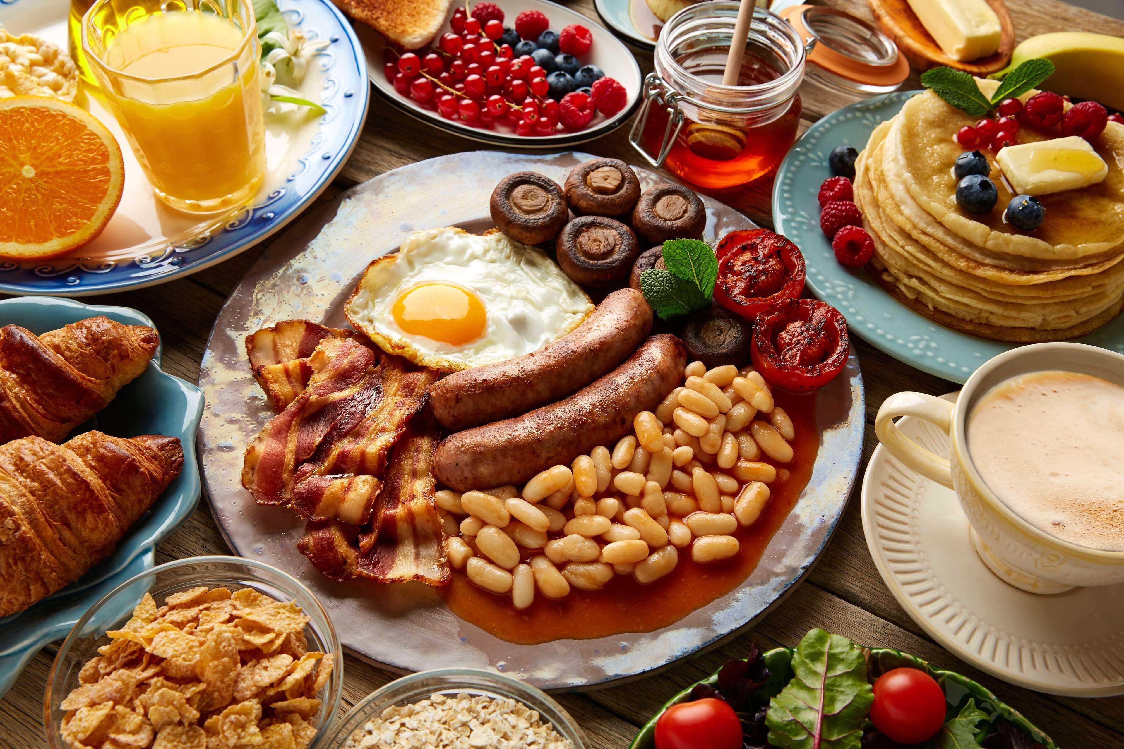 A breakfast spread with eggs, sausages, beans, toast, and various fruits.