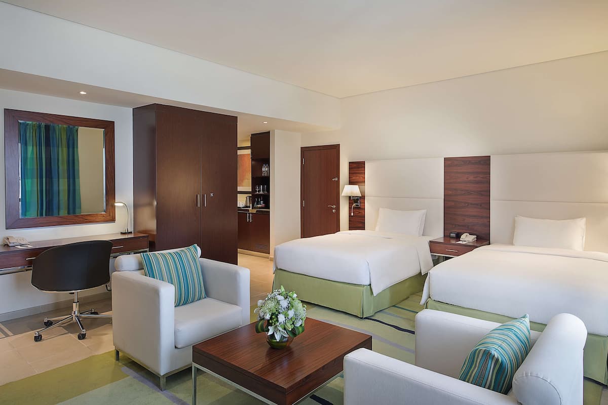 A hotel room with two beds, a desk, a chair, and a coffee table.