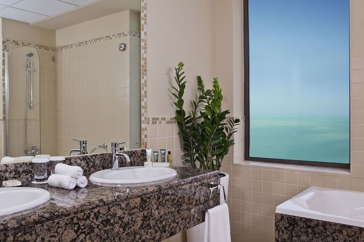 A bathroom with a large mirror, two sinks, a shower, and a view of the ocean.
