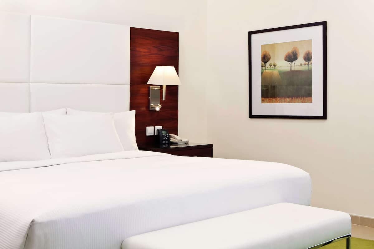 A neatly made bed with white linens, a wooden headboard, a bedside table with a lamp, and a framed picture on the wall.