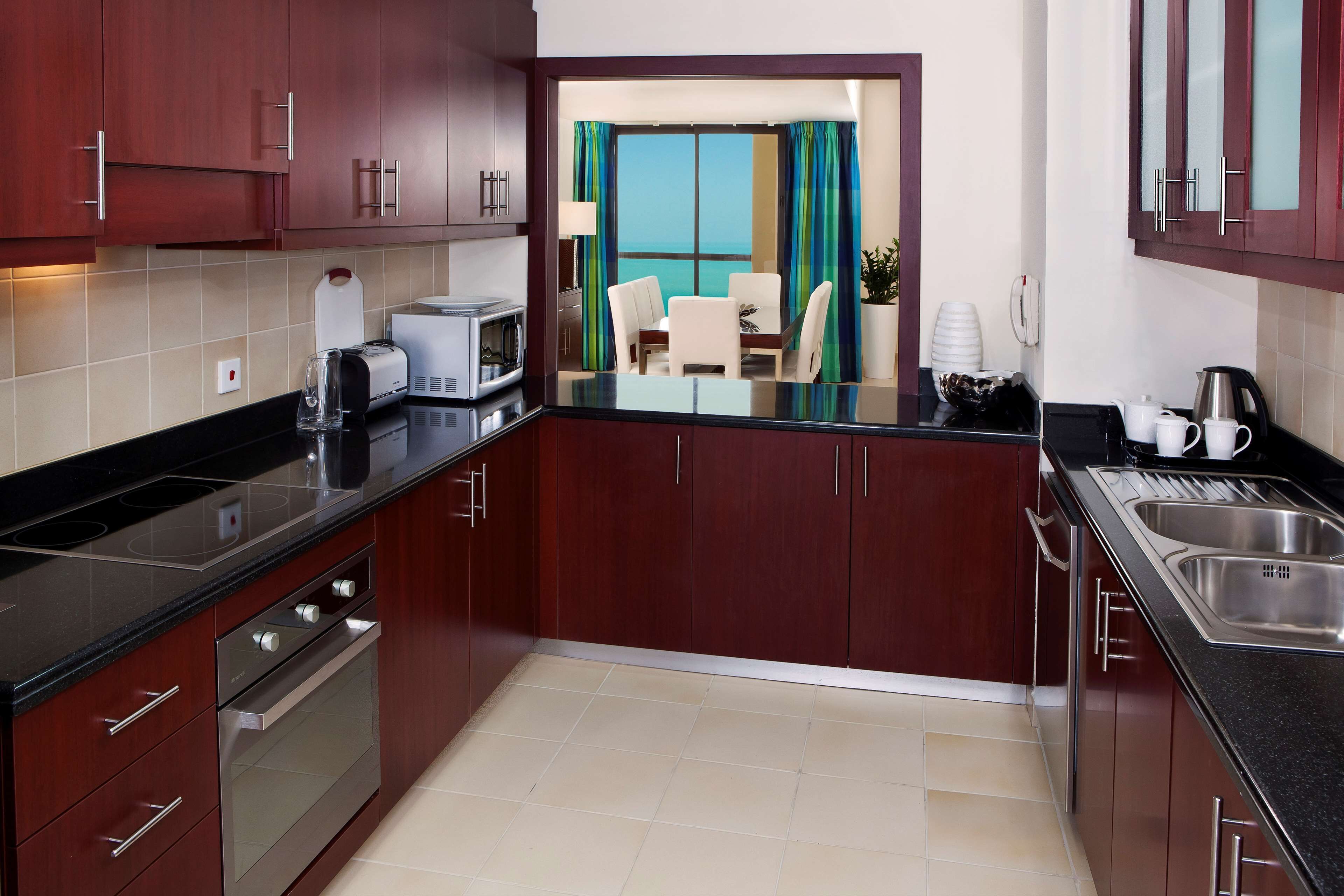 A modern kitchen with dark wooden cabinets, stainless steel appliances, and a view to a balcony with a table and chairs.
