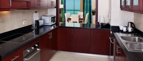 A modern kitchen with dark wooden cabinets, stainless steel appliances, and a view to a balcony with a table and chairs.