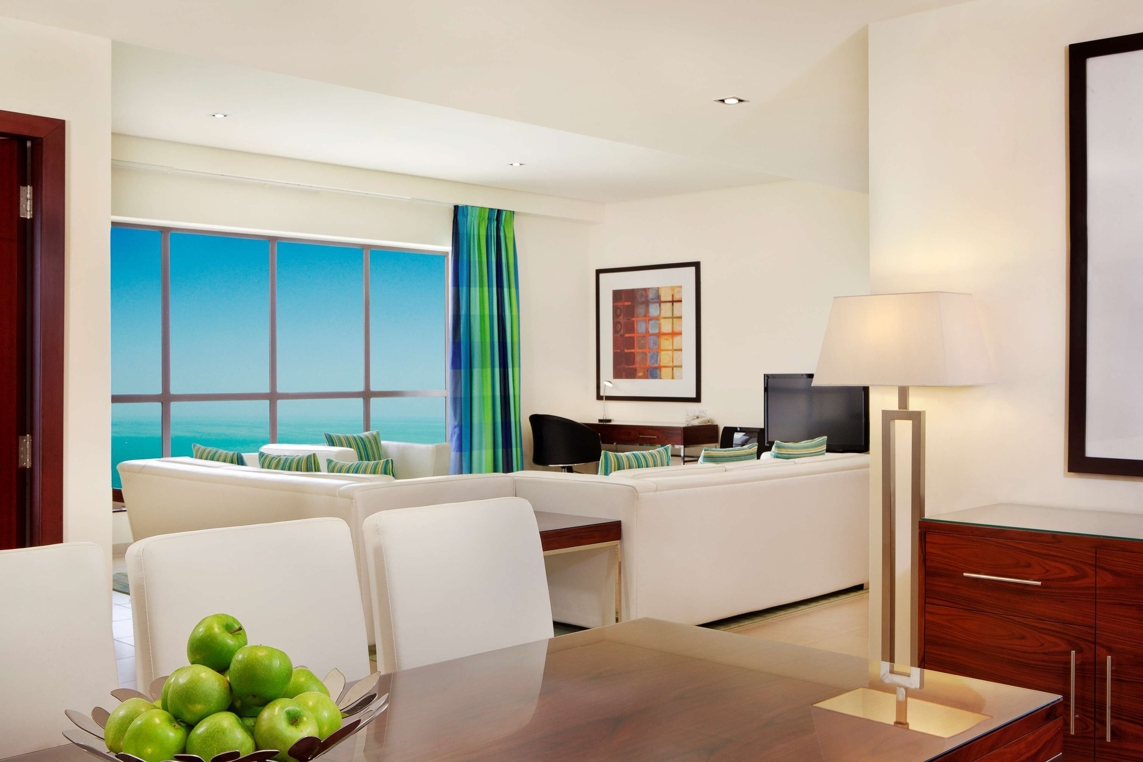 Ein modernes Hotelzimmer mit Essbereich, einer Sofagruppe, einem Fernseher und Blick auf den Ozean.