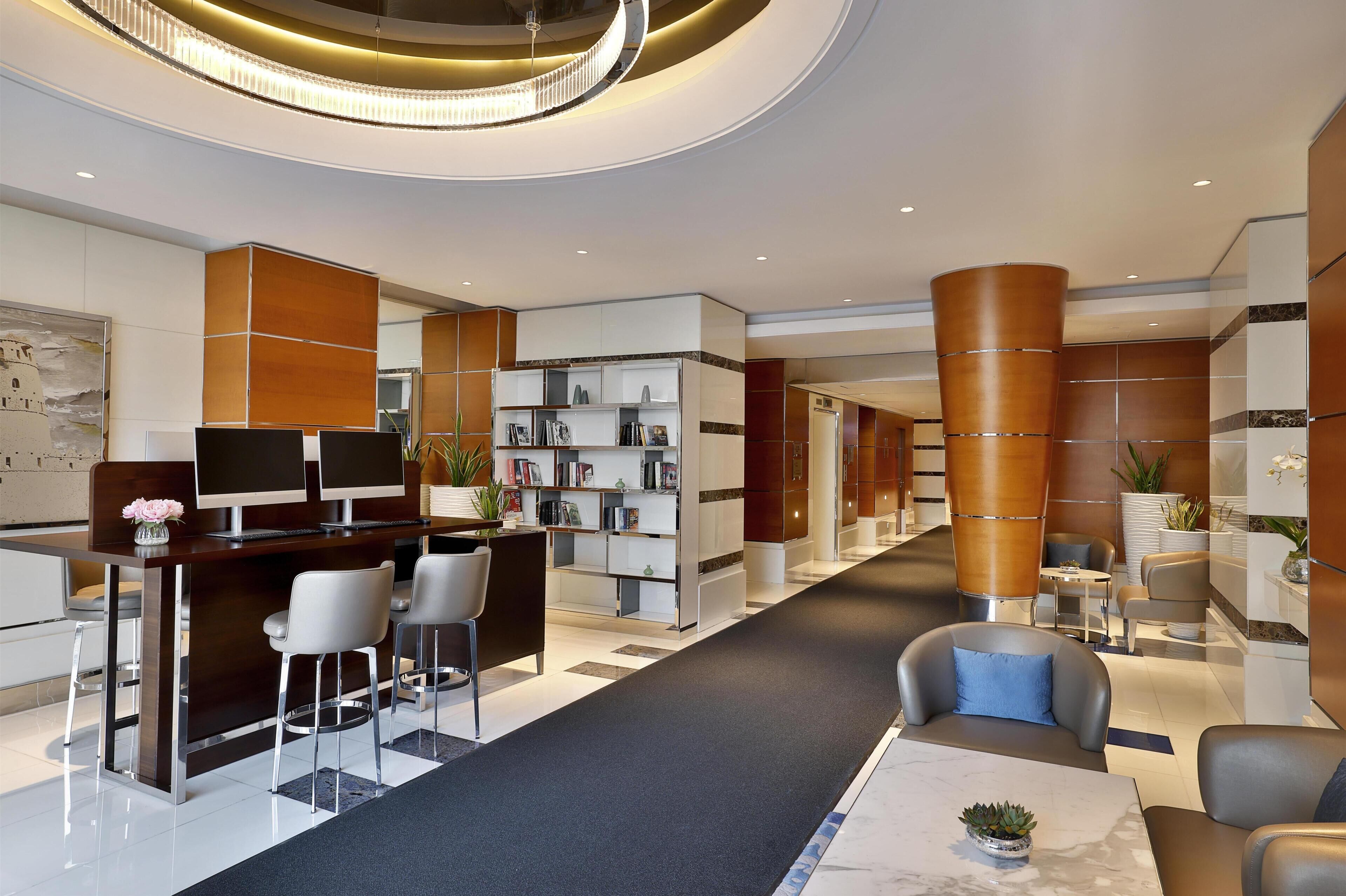 A modern hotel lobby with a reception desk, seating area, and a long corridor leading to other rooms.