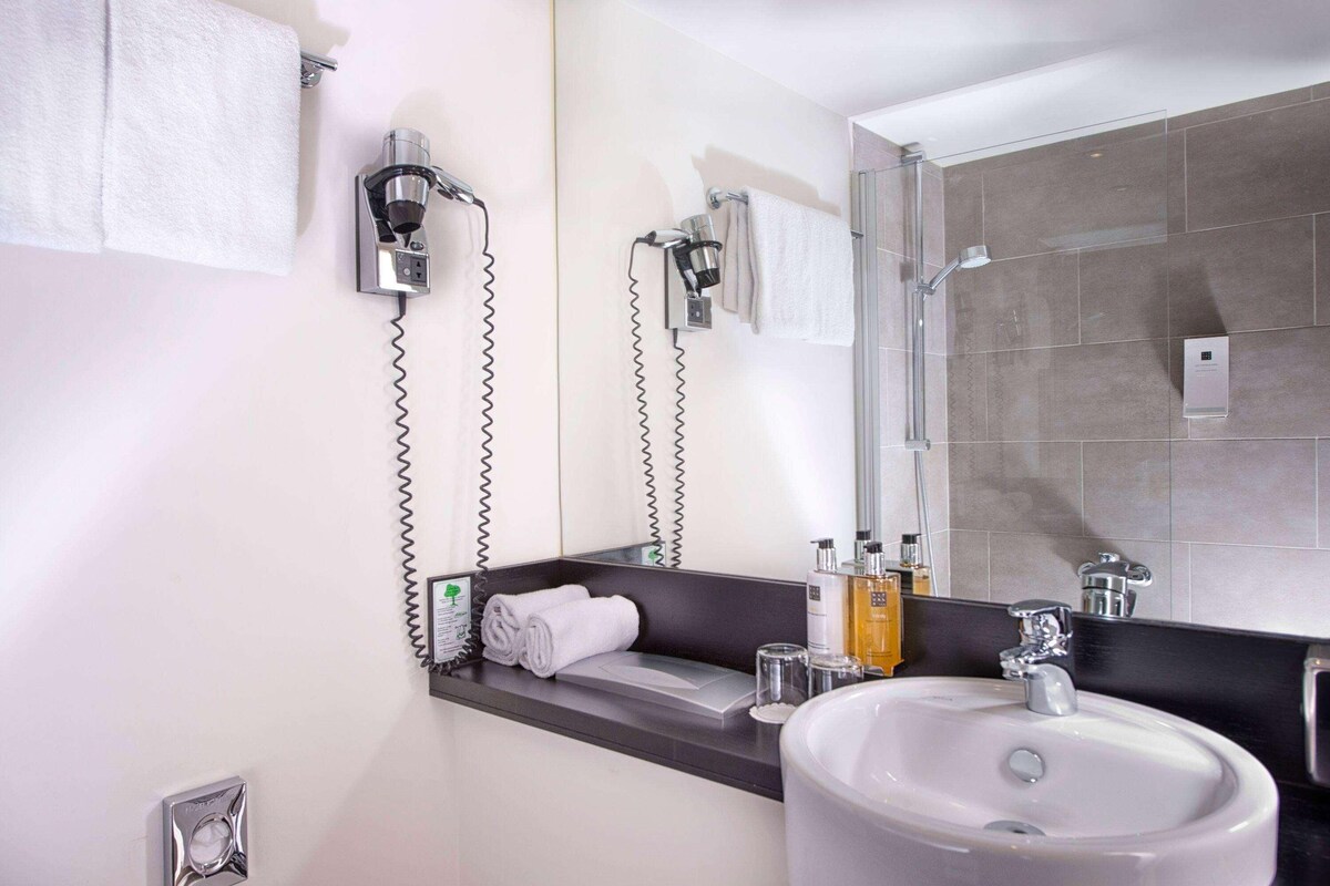 A modern bathroom with a sink, mirror, towel rack, and shower.