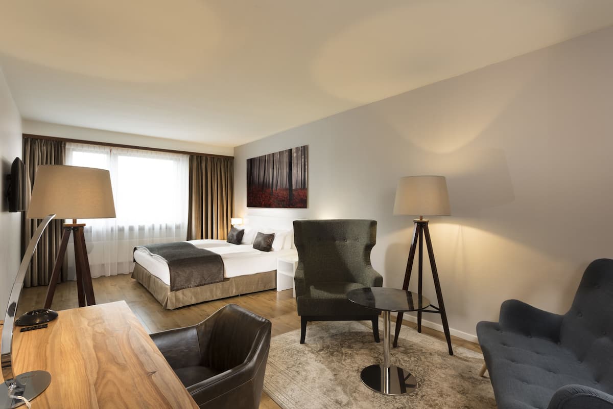 A hotel room with a bed, a desk, a chair, a lamp, and a painting on the wall.