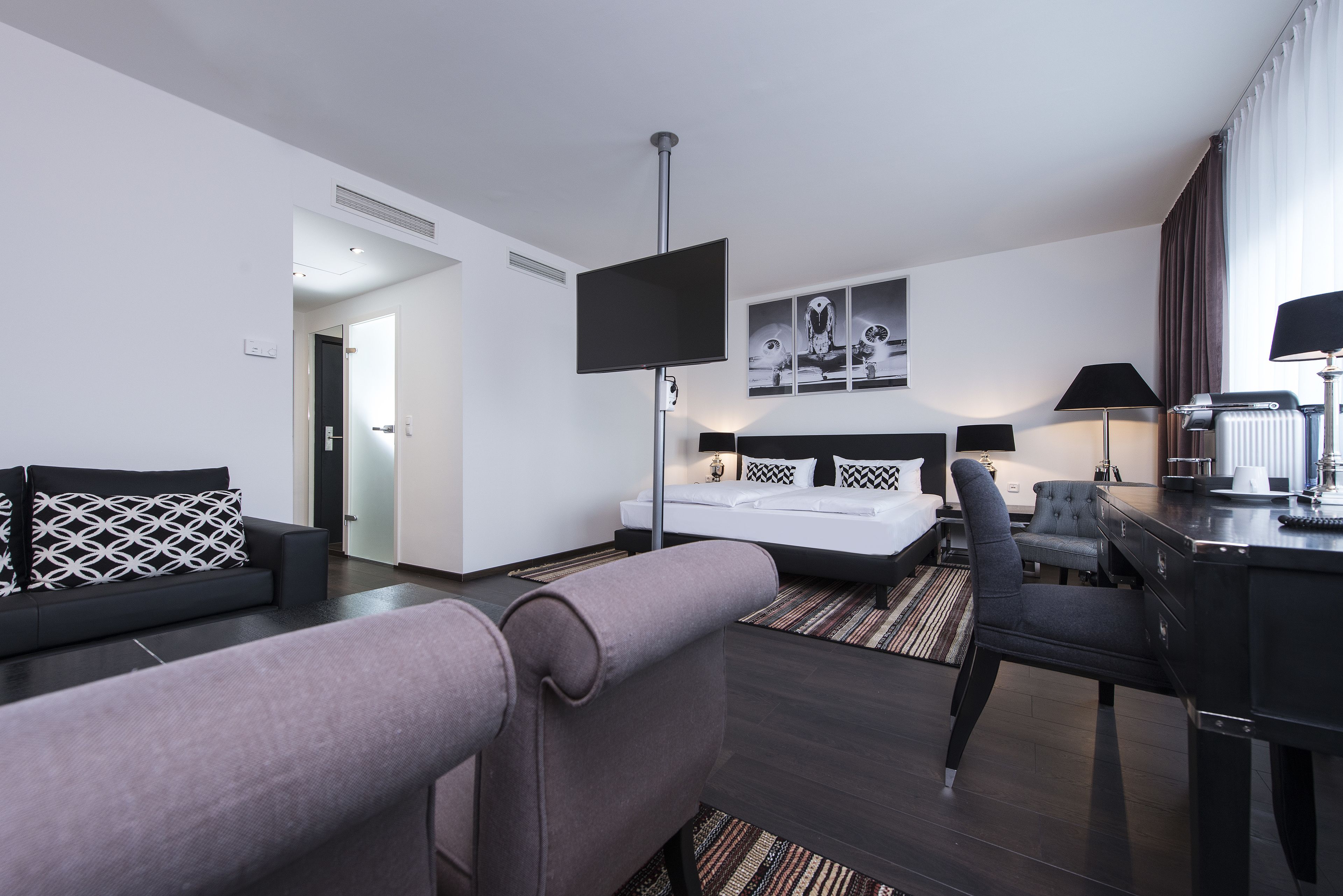 Ett modernt hotellrum med en säng, ett skrivbord, en stol, en TV och konstverk på väggen.