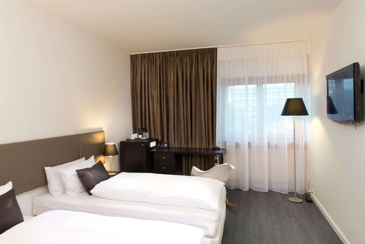 Habitación de hotel con dos camas, un escritorio, una silla, un televisor y una ventana con cortinas.