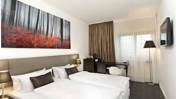 A hotel room with a large bed, a desk, a chair, a flat-screen TV, and a painting of a forest.
