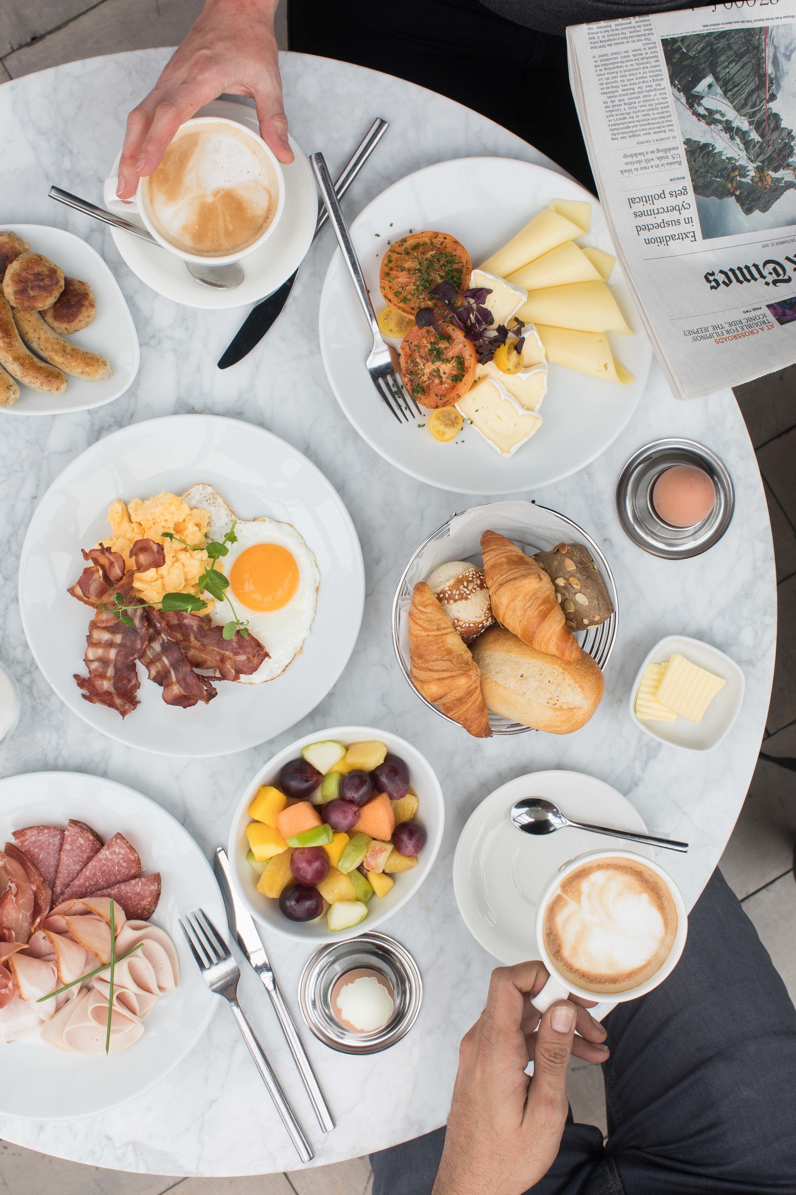 Un desayuno con platos de huevos, tocino, croissants y fruta.