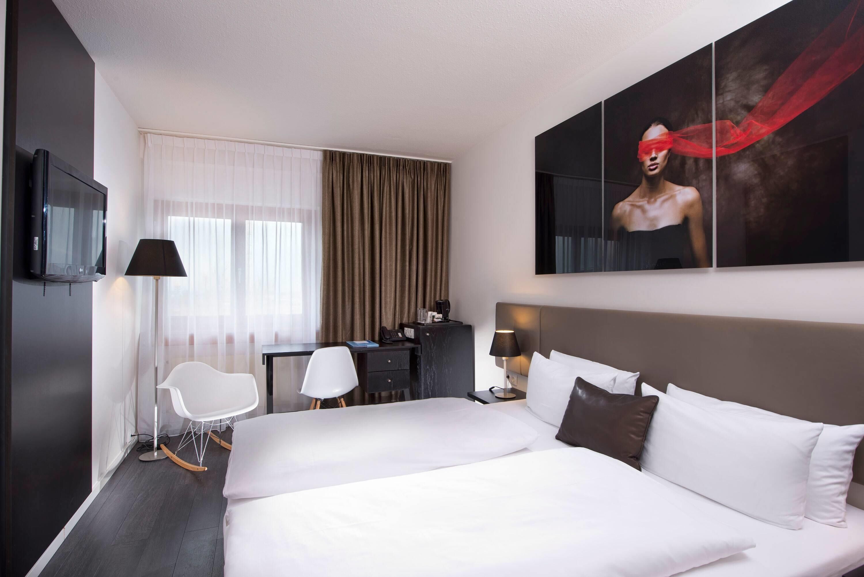 Habitación de hotel con una cama grande, un escritorio, una silla, un televisor y un cuadro en la pared.