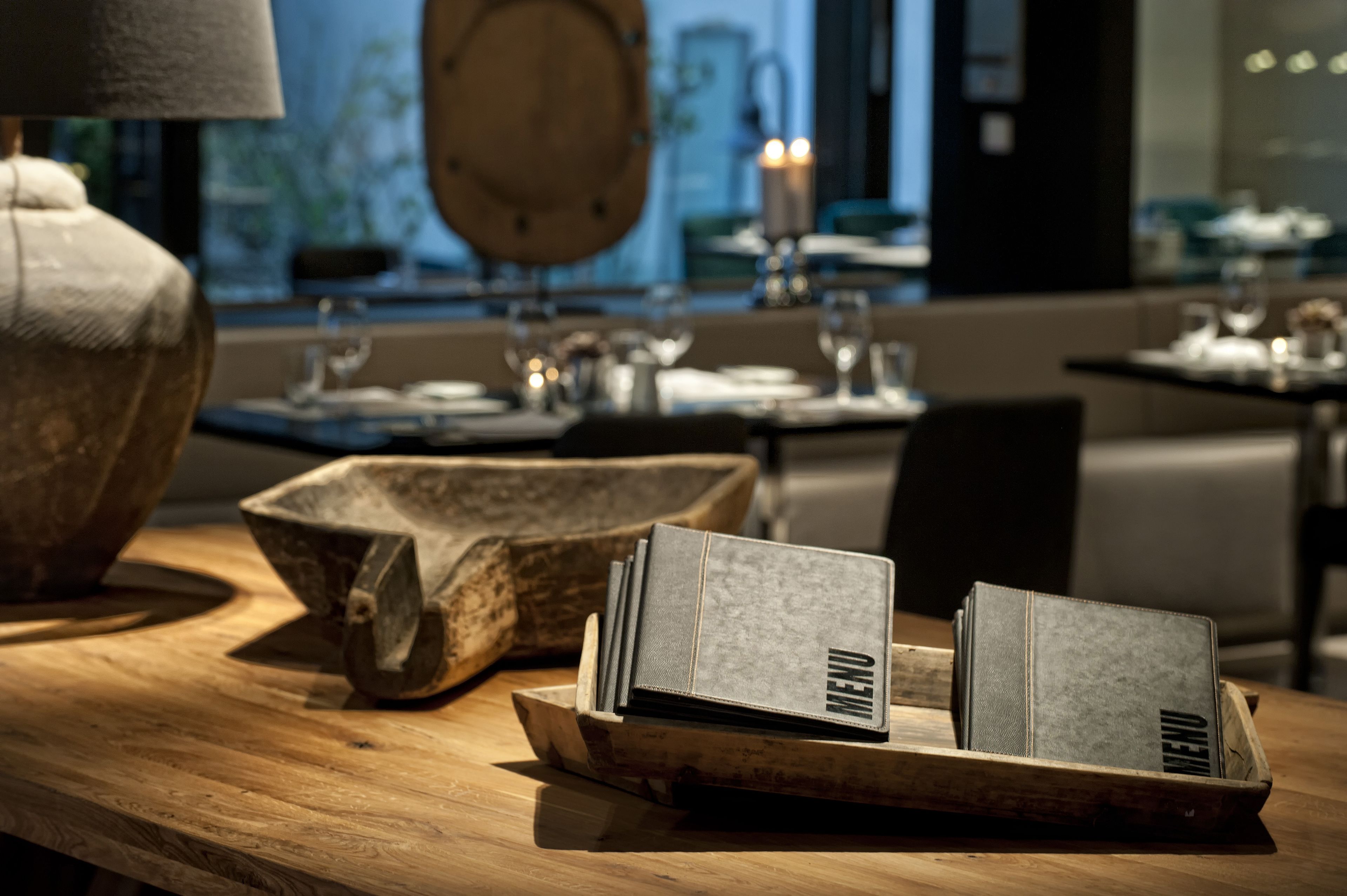 A wooden table with a menu, a vintage lamp, and a rustic bowl.