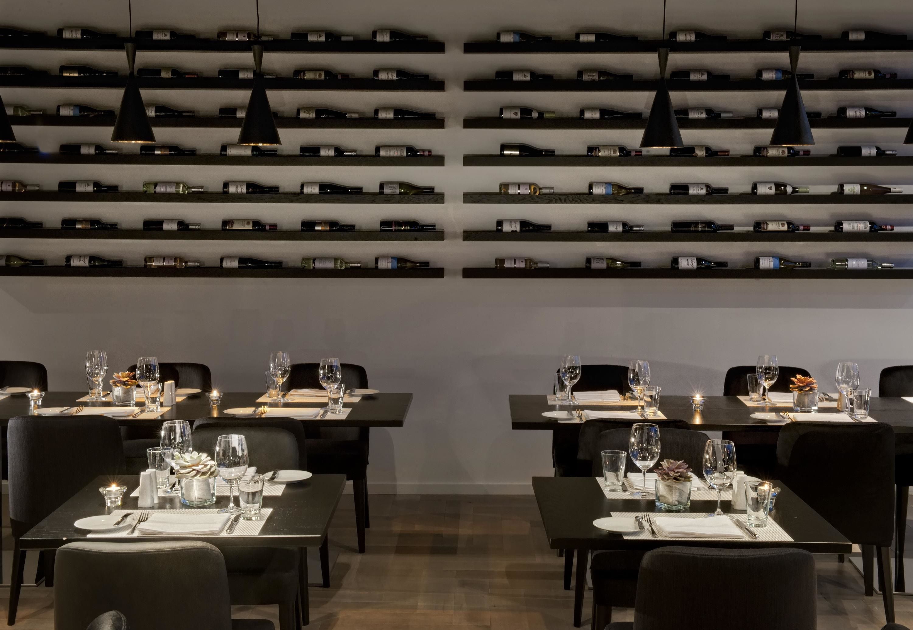 A restaurant with multiple tables set for dining, each with wine bottles on the wall behind.