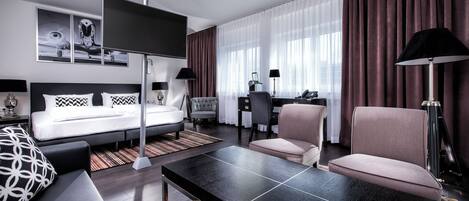 A modern hotel room with a bed, a desk, a chair, a sofa, and a TV.