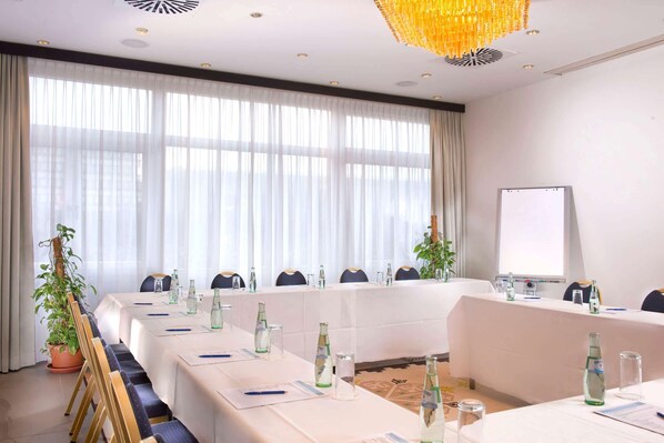 A conference room with a long table, chairs, a whiteboard, and a large window with curtains.
